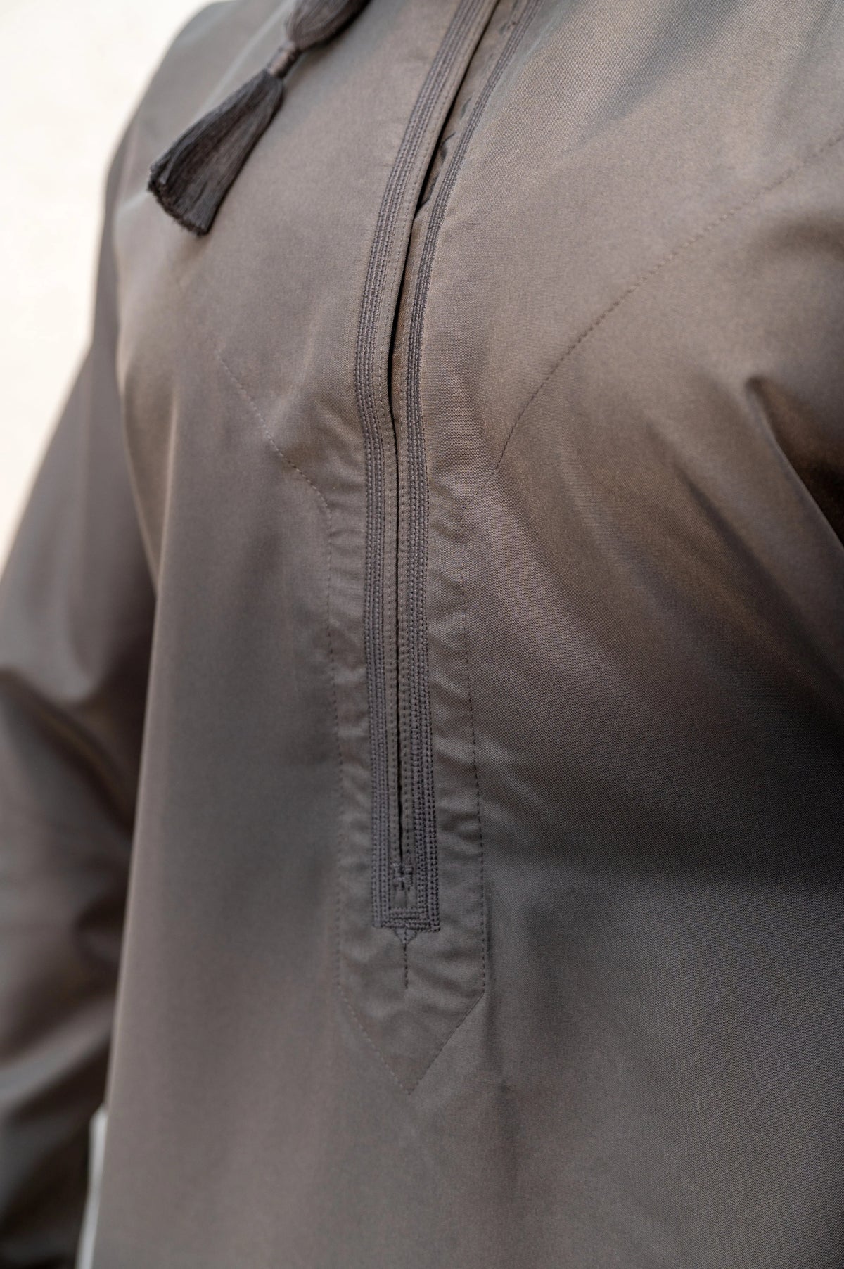 Close-up of chest embroidery and tassel on grey Omani thobe / jubba featuring detailed stitching and authentic handcrafted elements